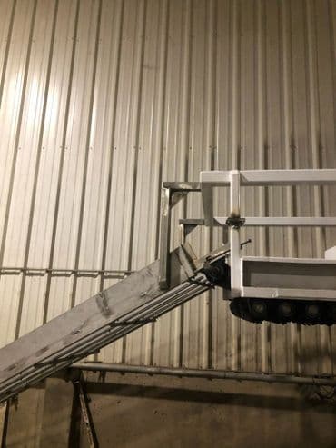 Industrial conveyor system with incline and metal railing against a corrugated wall.
