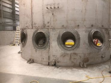 Large metal industrial tank with access ports in a warehouse setting.