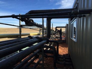Pipeline infrastructure with worker, showcasing industrial plumbing and machinery against blue sky.