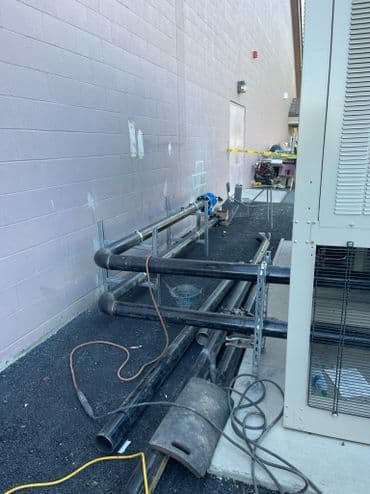 Pipes and construction equipment lined against a building exterior.