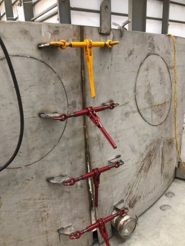 Industrial steel panel with red and yellow clamps for securing connections in a workshop setting.