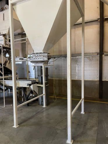 Industrial hopper and conveyor system in a warehouse setting, showcasing grain handling equipment.
