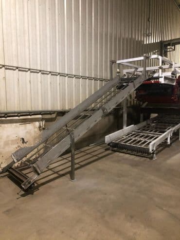 Metal loading ramp for vehicles in a warehouse with conveyor system nearby.
