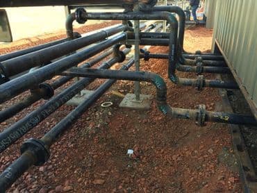 Industrial piping system with black pipes on gravel ground in construction site.