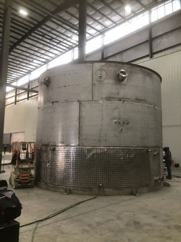 Large industrial stainless steel tank inside a warehouse under construction.
