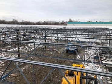 Steel structure framework of a construction site with equipment and snowy ground.
