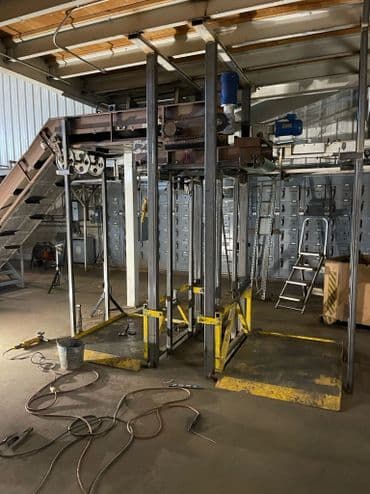 Industrial lifting equipment in a warehouse with metal framing and tools on the floor.