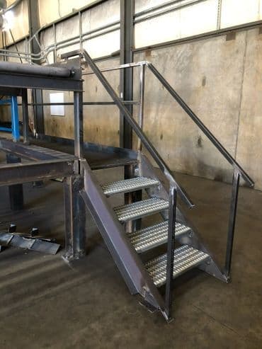 Steel staircase with handrail in a warehouse setting, showcasing industrial design and safety features.