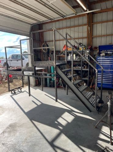 Metal staircase in a workshop, featuring handrails and a concrete floor.