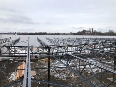 Partial view of metal framework for a new dock by a river, with snow on the ground.