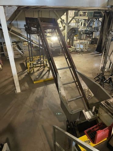 Industrial conveyor belt system in a warehouse, with metal frame and dim lighting.