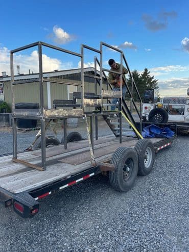 Worker assembling metal frame on trailer in outdoor worksite.