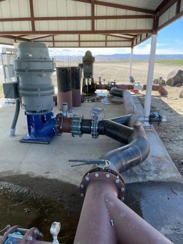 Industrial water pumping station with pipes, valves, and filtration equipment under a shed.