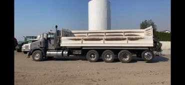 Gray dump truck parked on construction site with clear blue sky in background.