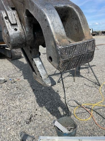 Heavy machinery arm with a metallic surface, showing wear and repair details on gravel site.