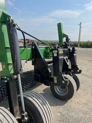 Close-up of agricultural machinery with hydraulic components and large wheels on gravel road.