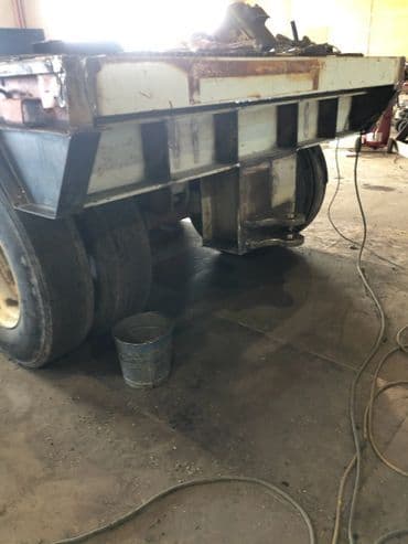 Rear view of a heavy-duty truck with worn tires, parked in a workshop with tools nearby.