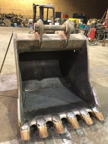 Industrial excavator bucket in a warehouse, highlighting teeth and sturdy construction.