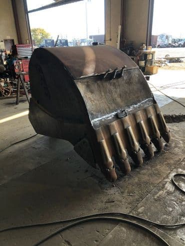 Excavator bucket in workshop, showcasing heavy-duty construction equipment for repair.