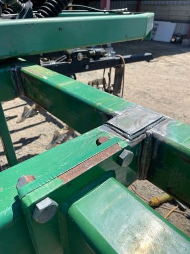 Close-up of welded metal frame with bolts on a green agricultural machine component.