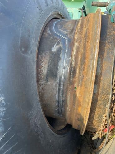 Close-up of a rusty tire rim with visible welding and wear on heavy machinery.