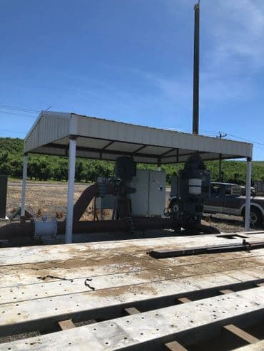 Water pumping station with protective cover and equipment on a worksite under clear blue sky.