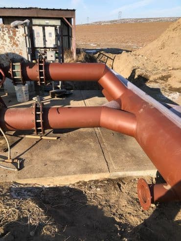 Brown industrial pipes connected at a pump station in a rural landscape.