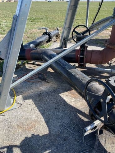 Black industrial pipes and valves positioned on a concrete surface in a grassy area.