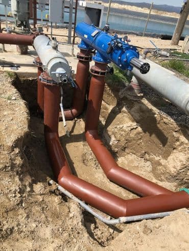 Brown pipes and blue valve installed in a trench at a construction site near water.