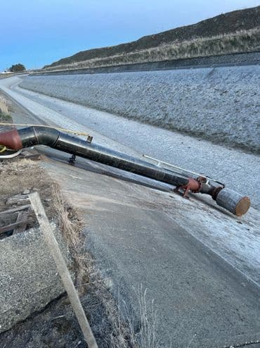 Pipe structure next to a dry canal, with a gravel bank and distant vegetation.