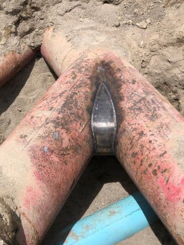 Repair of a large underground pipe joint with welded metal and surrounded by sand.