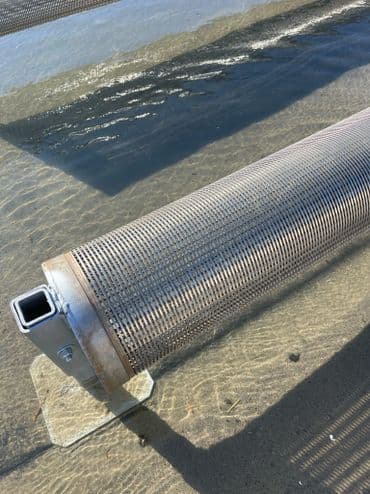 Metal cylindrical filter in shallow water, showcasing textured surface and structural details.