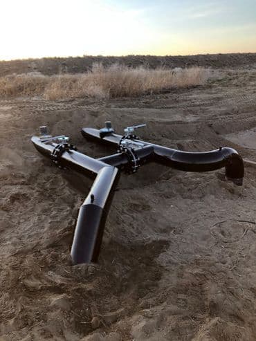 Black irrigation pipes lying in sandy terrain under a clear sky at sunset.