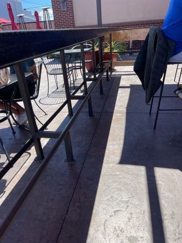 Outdoor seating area with metal railing and shadows from sunlight. Casual dining ambiance.