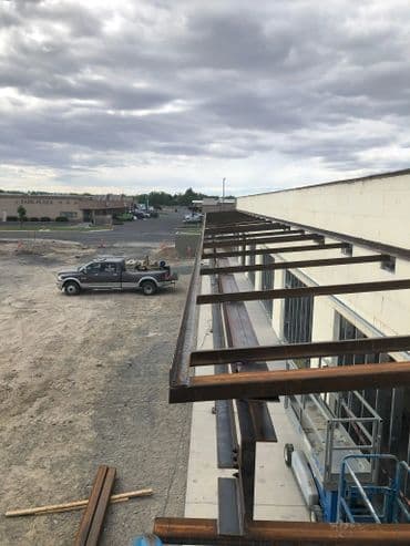 Construction site featuring steel beams and a pickup truck in the background under a cloudy sky.