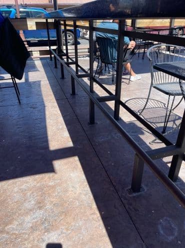 Outdoor dining area with metal railings and tables, featuring a seated person in the background.