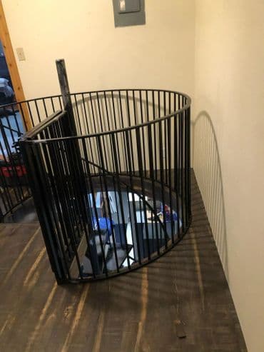 Spiral staircase railing in a modern interior with wooden floor and wall lights.