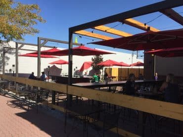 Outdoor dining area with red umbrellas and seating under clear blue skies.