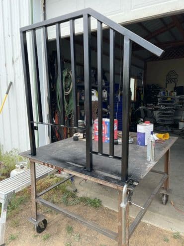 Black metal railing on a work table in a workshop, tools and materials in background.