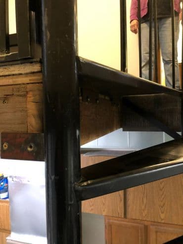 Metal staircase with wooden steps and a person standing on the upper level.