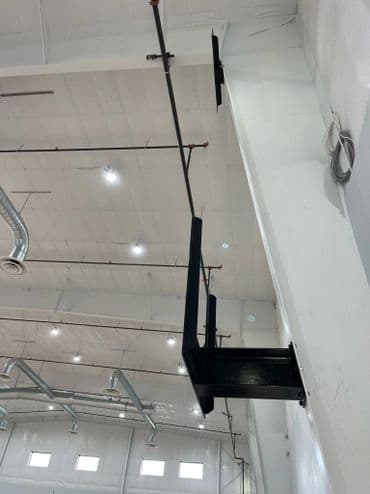 Industrial ceiling structure with black support beams and overhead lights in a spacious facility.