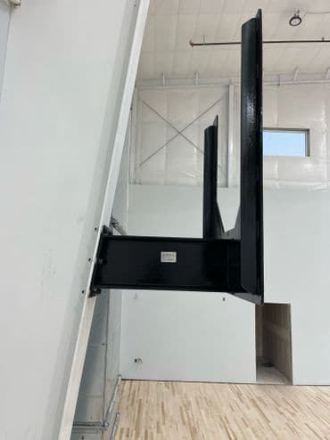 Vertical basketball hoop mounted on a wall in a gym with wooden flooring.