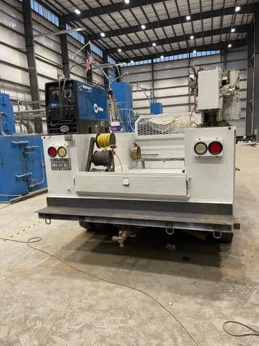Rear view of a white utility truck equipped with a crane in a spacious industrial setting.