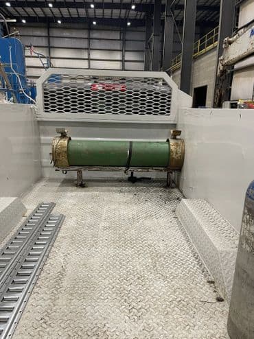 Interior view of a vehicle showing a green tank and textured flooring in a spacious industrial space.