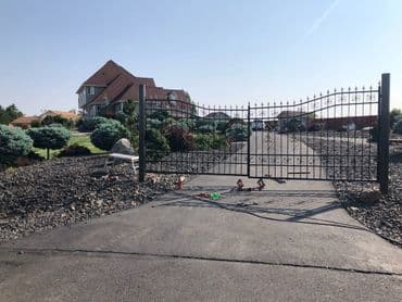 Elegant wrought iron gate leading to a spacious driveway and a large house surrounded by landscaping.