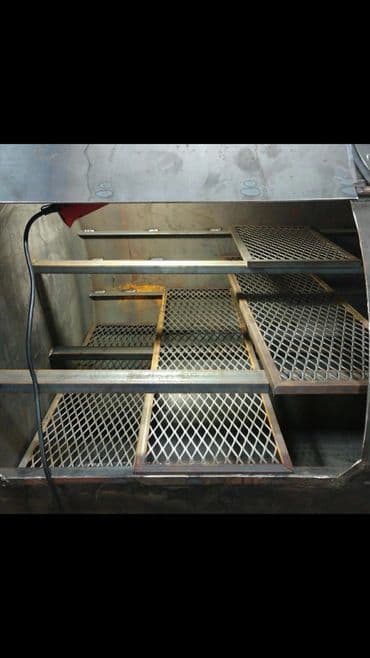 Industrial smoker interior showcasing metal racks with diamond mesh design for food preparation.
