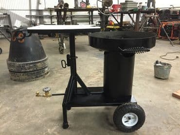 Portable black propane fryer with wheels and adjustable table in a workshop setting.