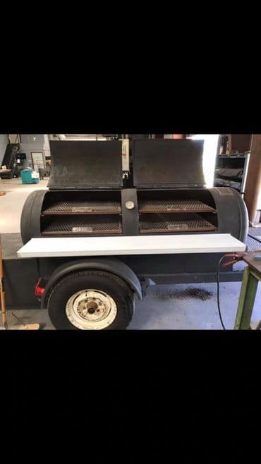 Black barbecue smoker grill on a trailer with dual cooking chambers and a white table surface.