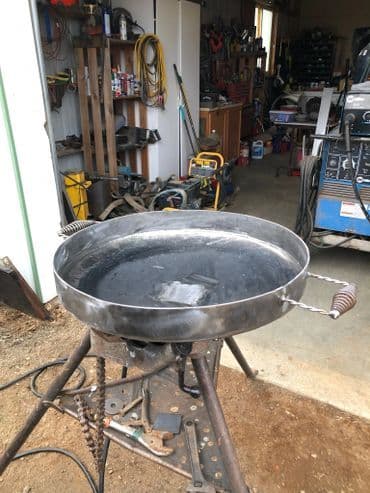 Metal cooking pan on a portable stand in a workshop with tools in the background.