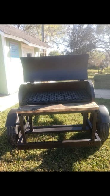 Custom-built charcoal grill with a wooden prep table, set on a grassy outdoor area.